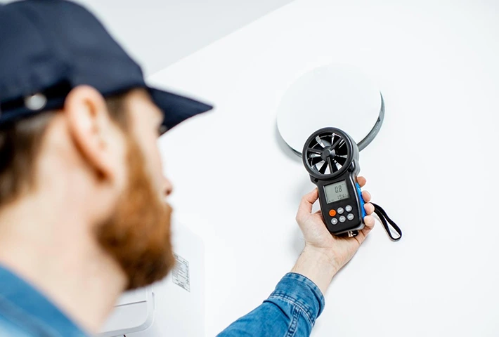 Technician using anemometer for indoor air quality testing on a vent.