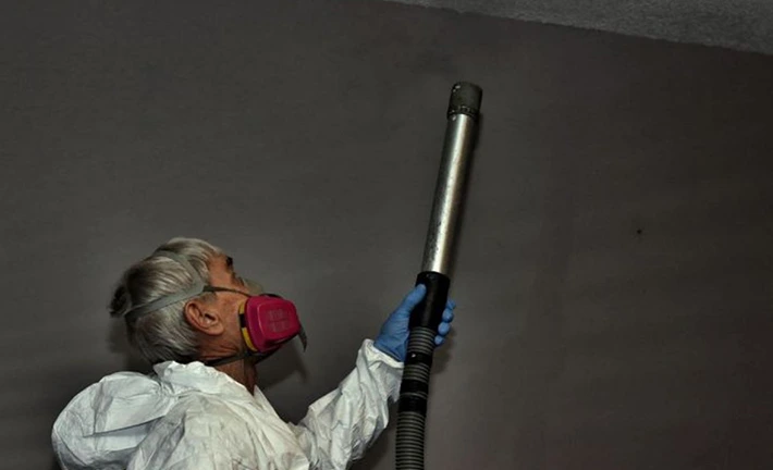 Worker in PPE inspecting air quality with testing equipment.