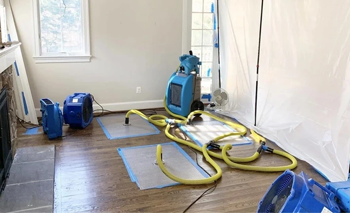 Home water extraction setup with dehumidifiers and air movers drying hardwood floors after a flood.