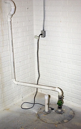 Sump pump system in a basement with white brick walls and a concrete floor.