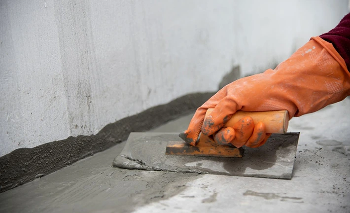 Applying concrete foundation repair with trowel and gloved hand, close-up.