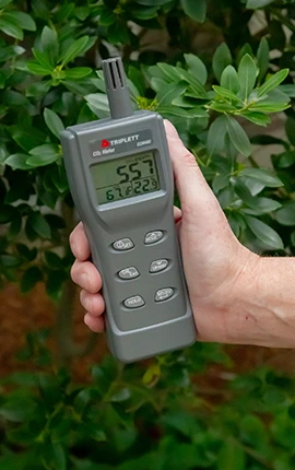 Hand holding a Triplett CO2 meter outdoors, displaying readings.