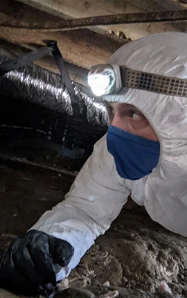 Inspector in hazmat suit examining crawl space for mold.