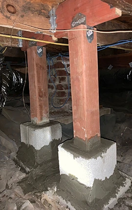 Crawl space with wooden support posts and concrete block foundation.