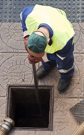 Worker in safety vest cleaning a sewer drain with a hose.