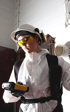 Technician in protective gear using a device to analyze a building. Local Experts.