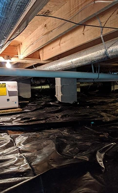 Crawl space with black plastic liner, support piers, and HVAC ductwork. Pier & beam repair may be needed.