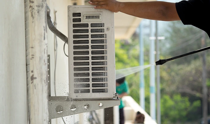Technician pressure washing an air conditioner coil for Coil & Blower Motor Cleaning.