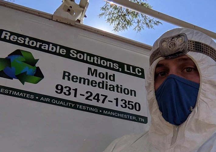 Mold remediation specialist in protective gear next to Restorable Solutions truck, phone 931-247-1350.