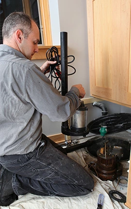 Man repairing a sump pump, kneeling on a tarp.