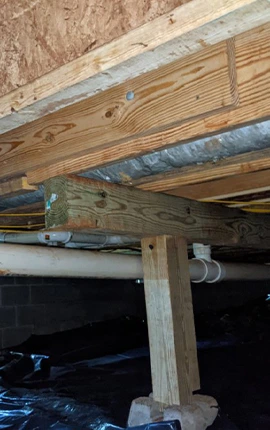 Crawl space with wood beam support under floor joists.