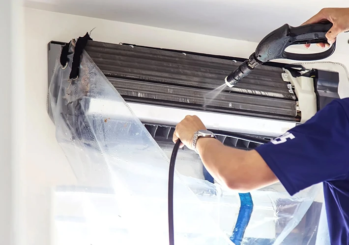 Technician cleaning an HVAC system with a power washer for sanitation.