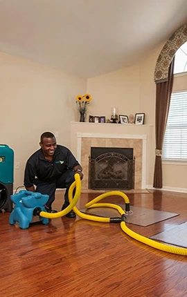Technician using water extraction equipment to remove water from hardwood floor after flooding.